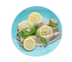 Photo of Blue plate with delicious salted herring fillets, basil, lemon slices and peppercorns isolated on white, top view