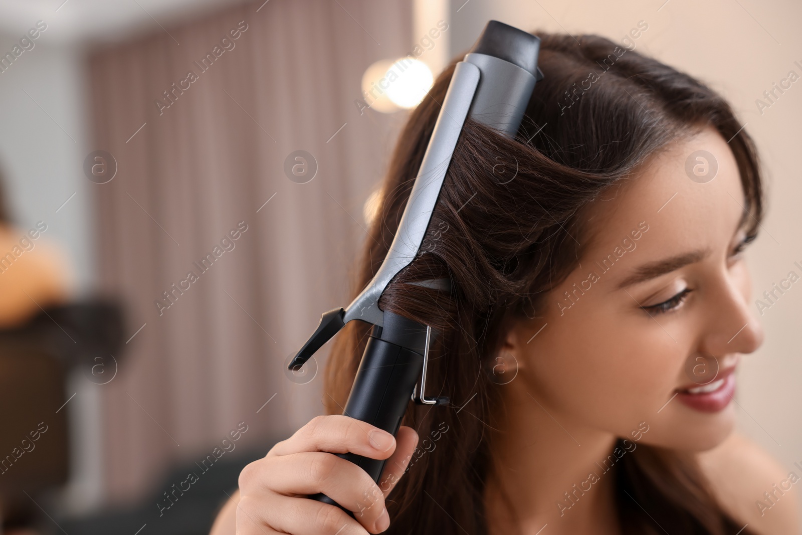 Photo of Beautiful woman using curling hair iron indoors. Space for text