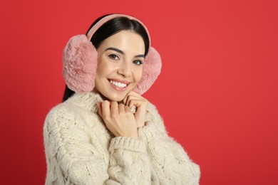 Beautiful young woman wearing earmuffs on red background. Space for text