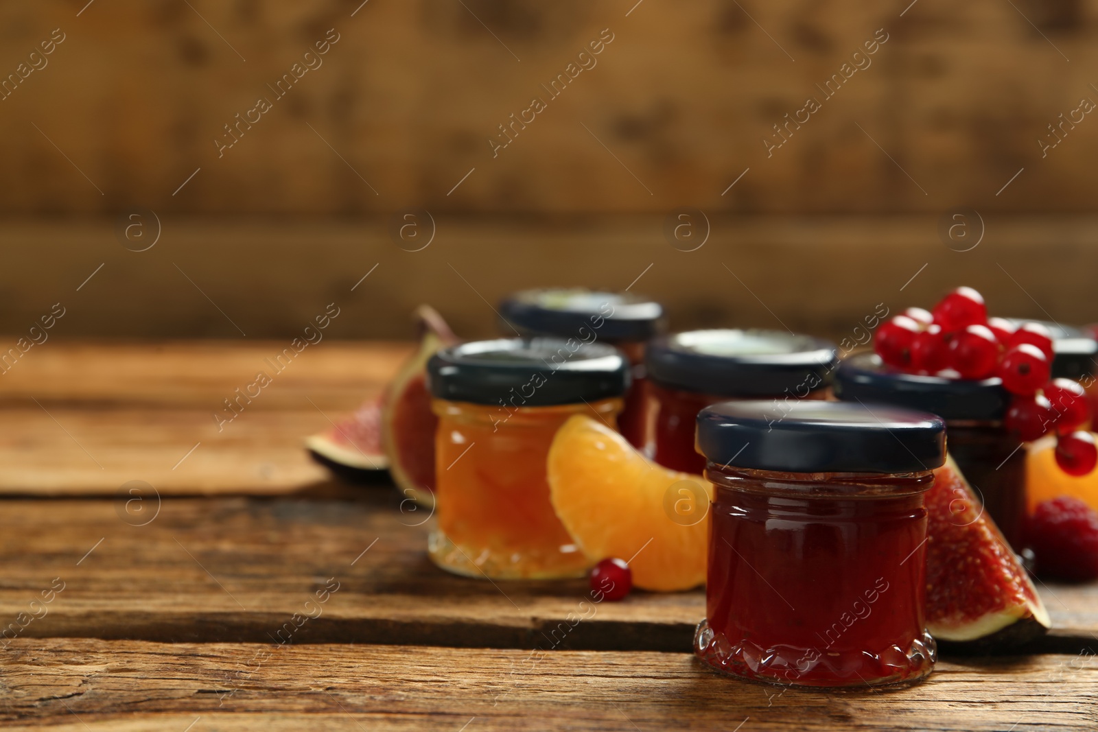 Photo of Jars of different jams and fresh ingredients on wooden table, space for text