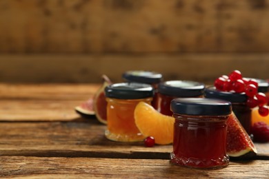Jars of different jams and fresh ingredients on wooden table, space for text