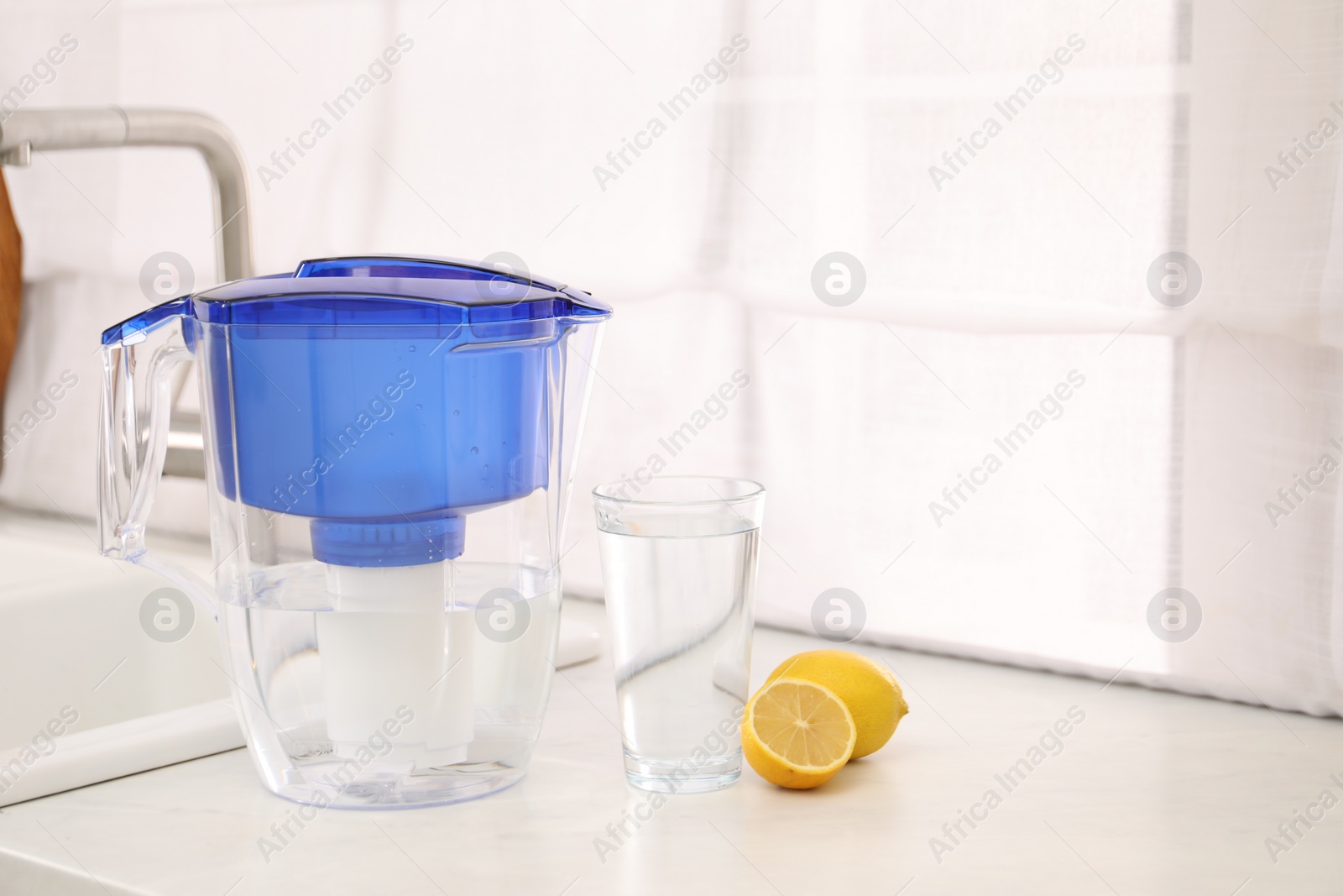 Photo of Water filter jug, glass and lemons on countertop in kitchen, space for text