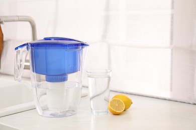 Photo of Water filter jug, glass and lemons on countertop in kitchen, space for text