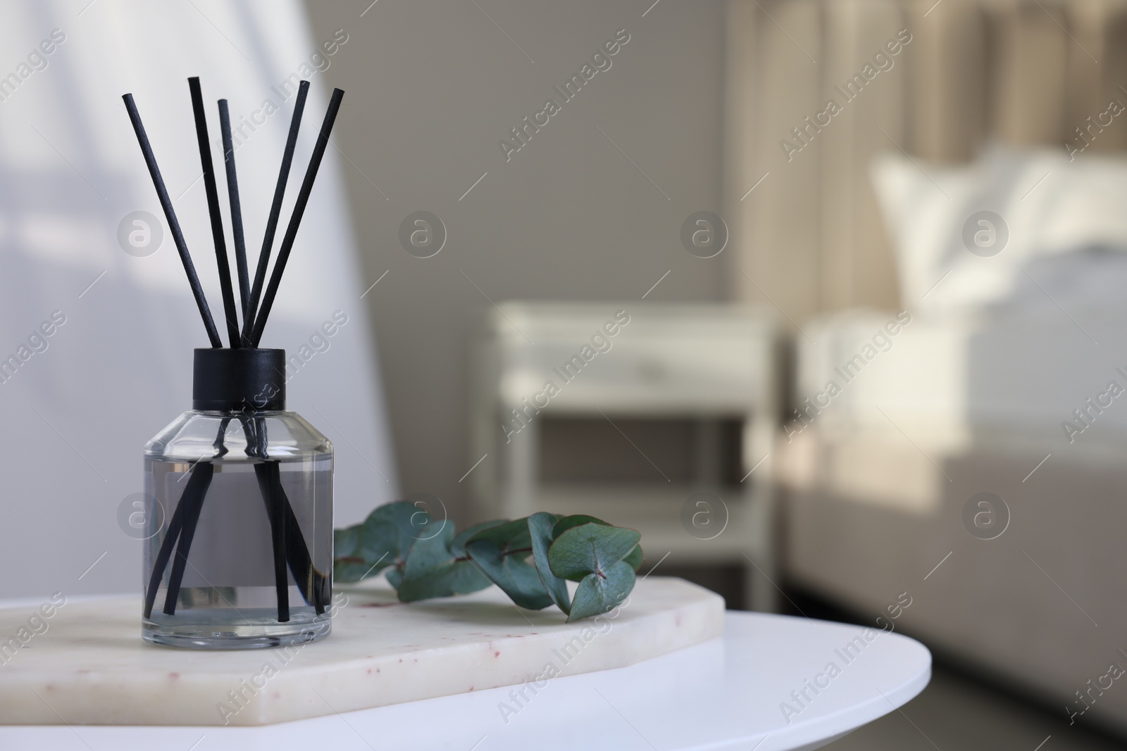 Photo of Aromatic reed air freshener and eucalyptus branch on white table in bedroom, space for text