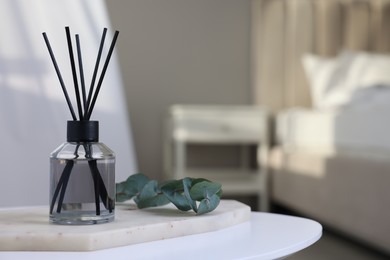 Aromatic reed air freshener and eucalyptus branch on white table in bedroom, space for text