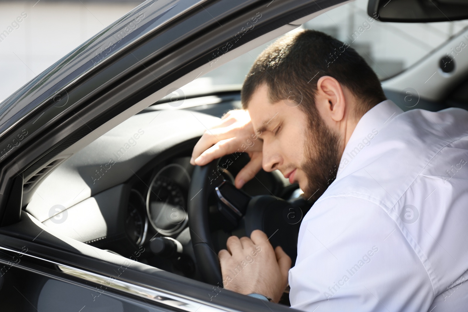 Photo of Tired man sleeping on steering wheel in his modern car