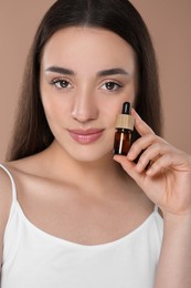 Photo of Beautiful young woman with bottle of essential oil on brown background