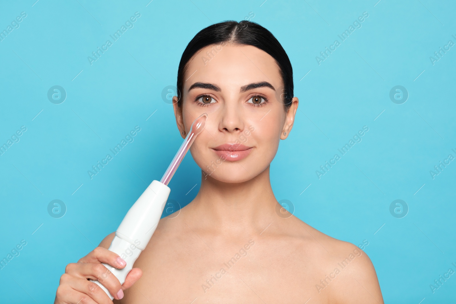 Photo of Woman using high frequency darsonval device on light blue background