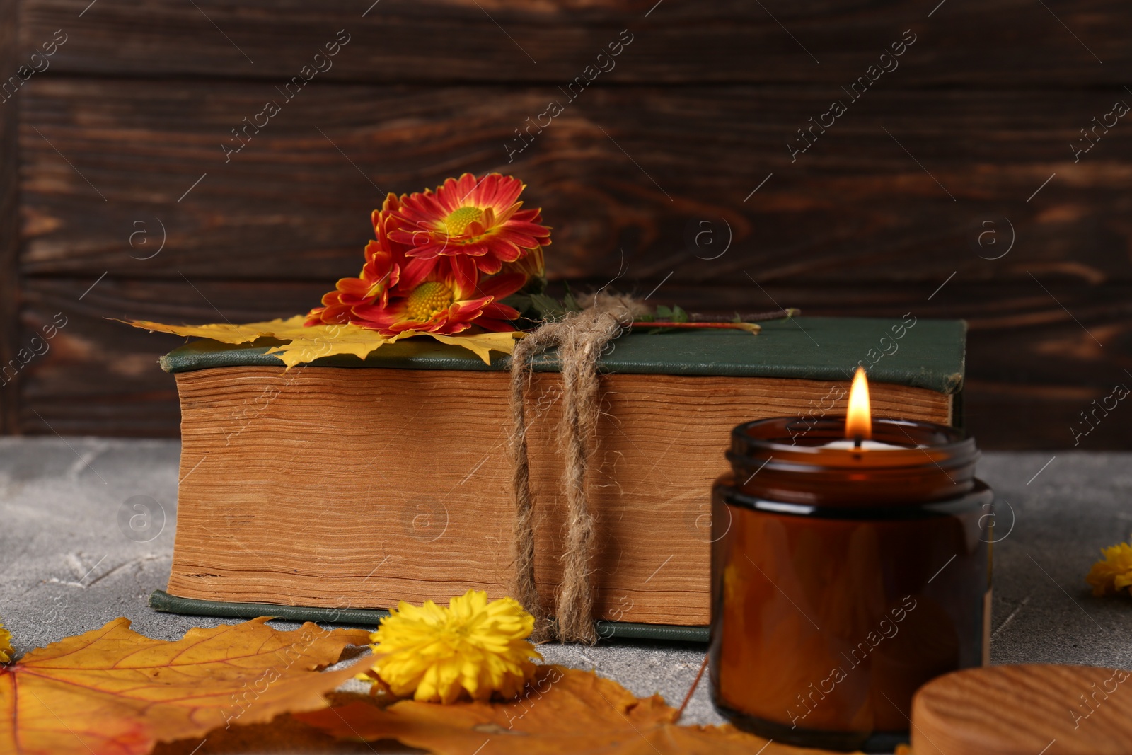 Photo of Book decorated with chrysanthemum flowers, autumn leaves and scented candle on light gray textured table