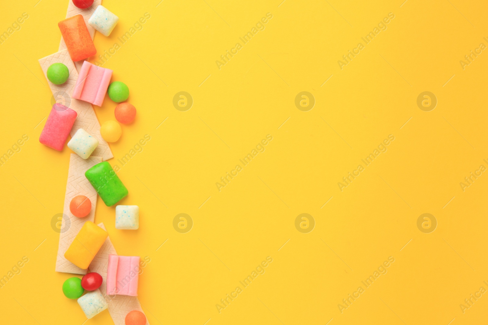 Photo of Many different chewing gums on yellow background, flat lay. Space for text