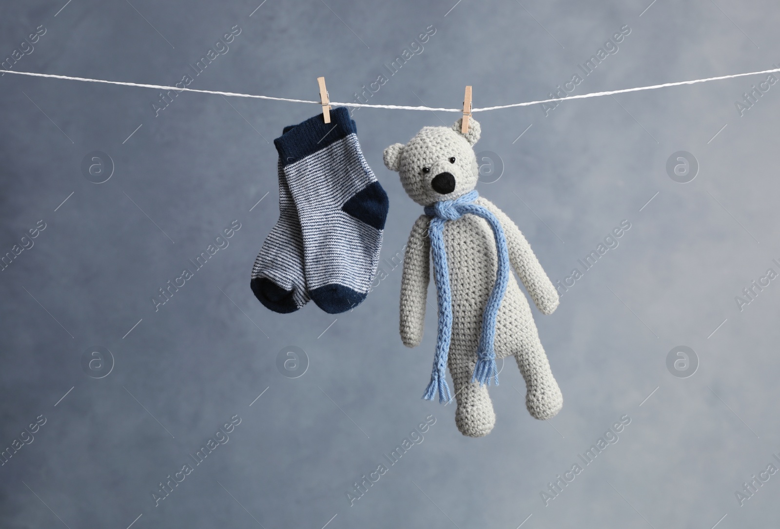 Photo of Pair of child's socks and toy bear hanging on laundry line against dark background