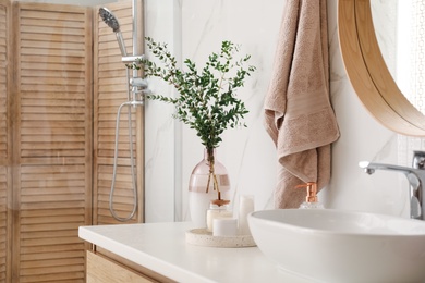 Photo of Vase with beautiful branches, candles and toiletries near vessel sink in bathroom. Interior design
