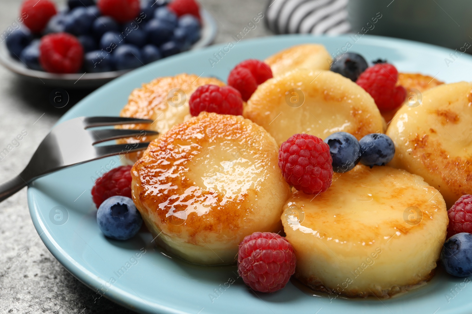 Photo of Delicious cottage cheese pancakes with fresh berries and honey on grey table, closeup