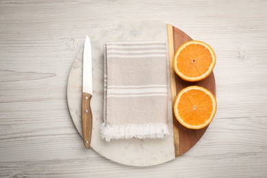 Cutting board with kitchen towel, halved orange and knife on white wooden table, top view