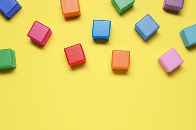 Blank colorful cubes on yellow background, flat lay. Space for text