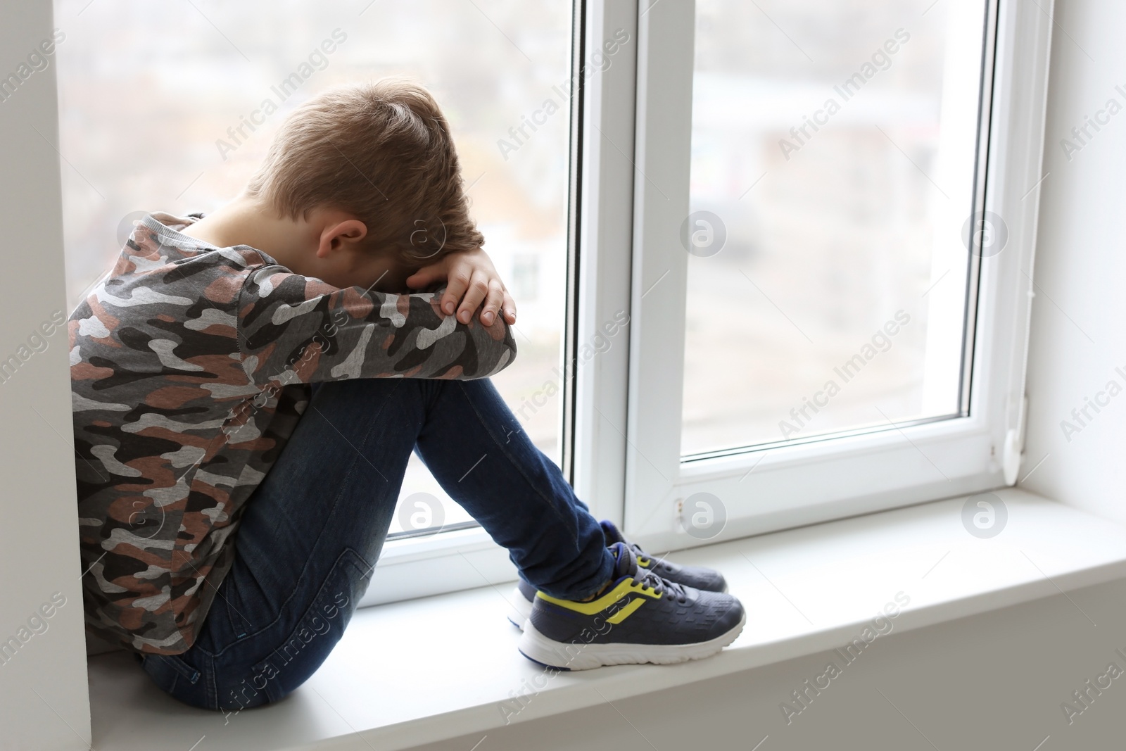 Photo of Lonely little boy near window indoors. Child autism