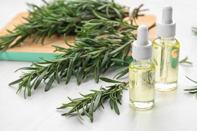 Fresh rosemary and bottles of essential oil on white table. Space for text