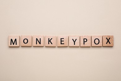 Photo of Word Monkeypox made of wooden squares on beige background, top view