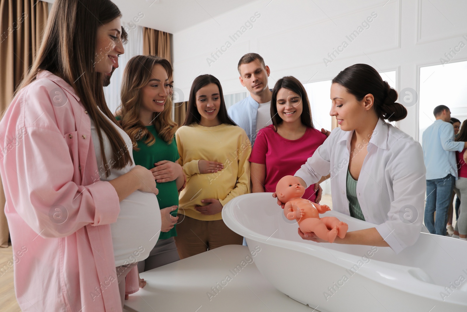 Photo of Pregnant women with men learning how to bathe baby at courses for expectant parents indoors