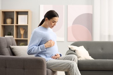 Photo of Pregnant young woman on armchair at home, space for text