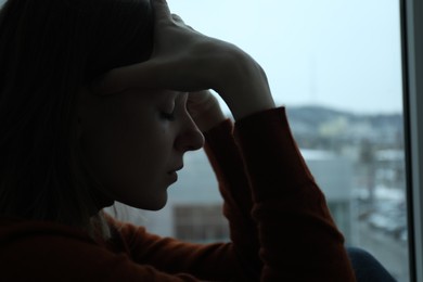 Photo of Sad young woman near window at home, closeup