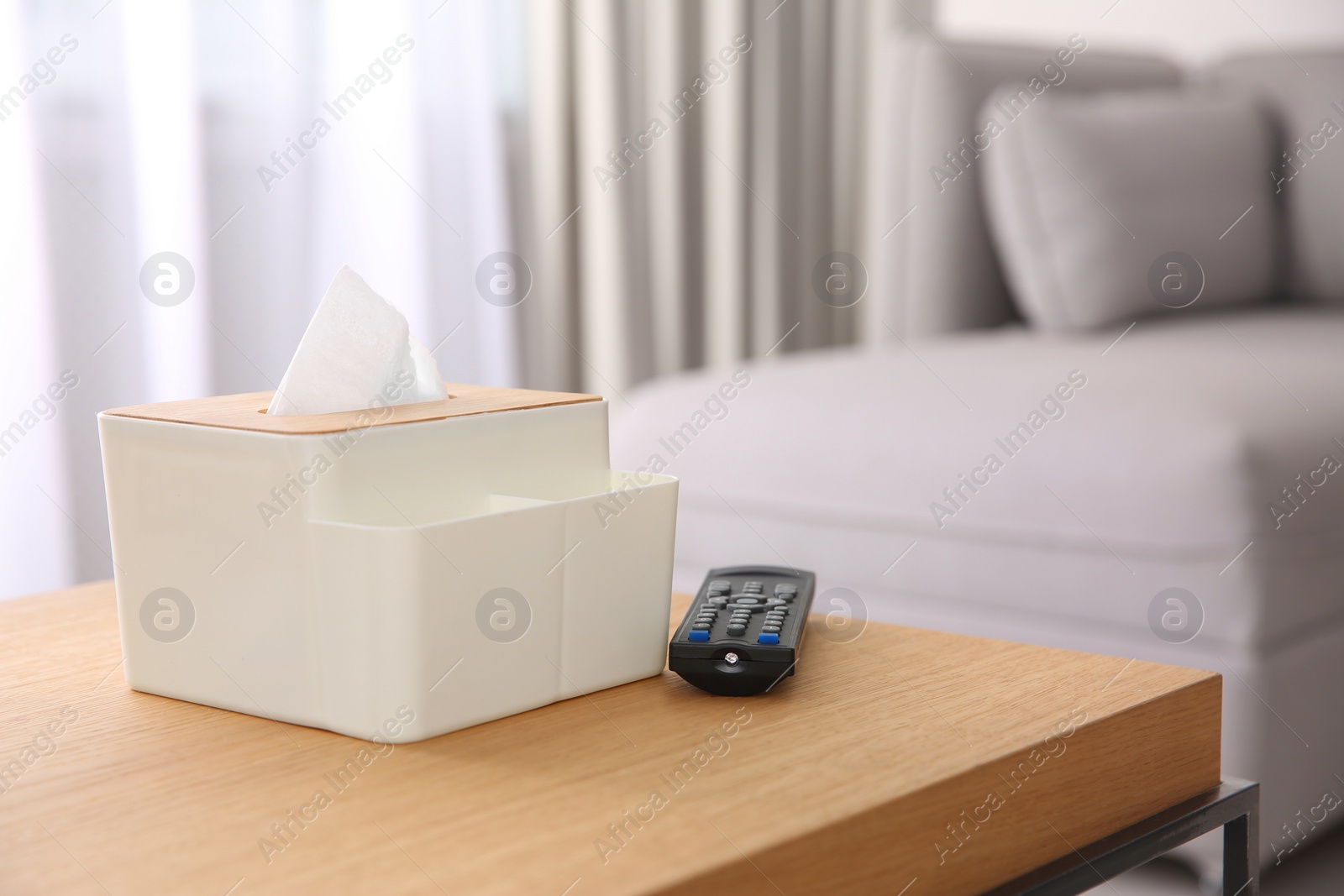 Photo of Box with paper tissues and TV remote control on wooden table in living room. Space for text