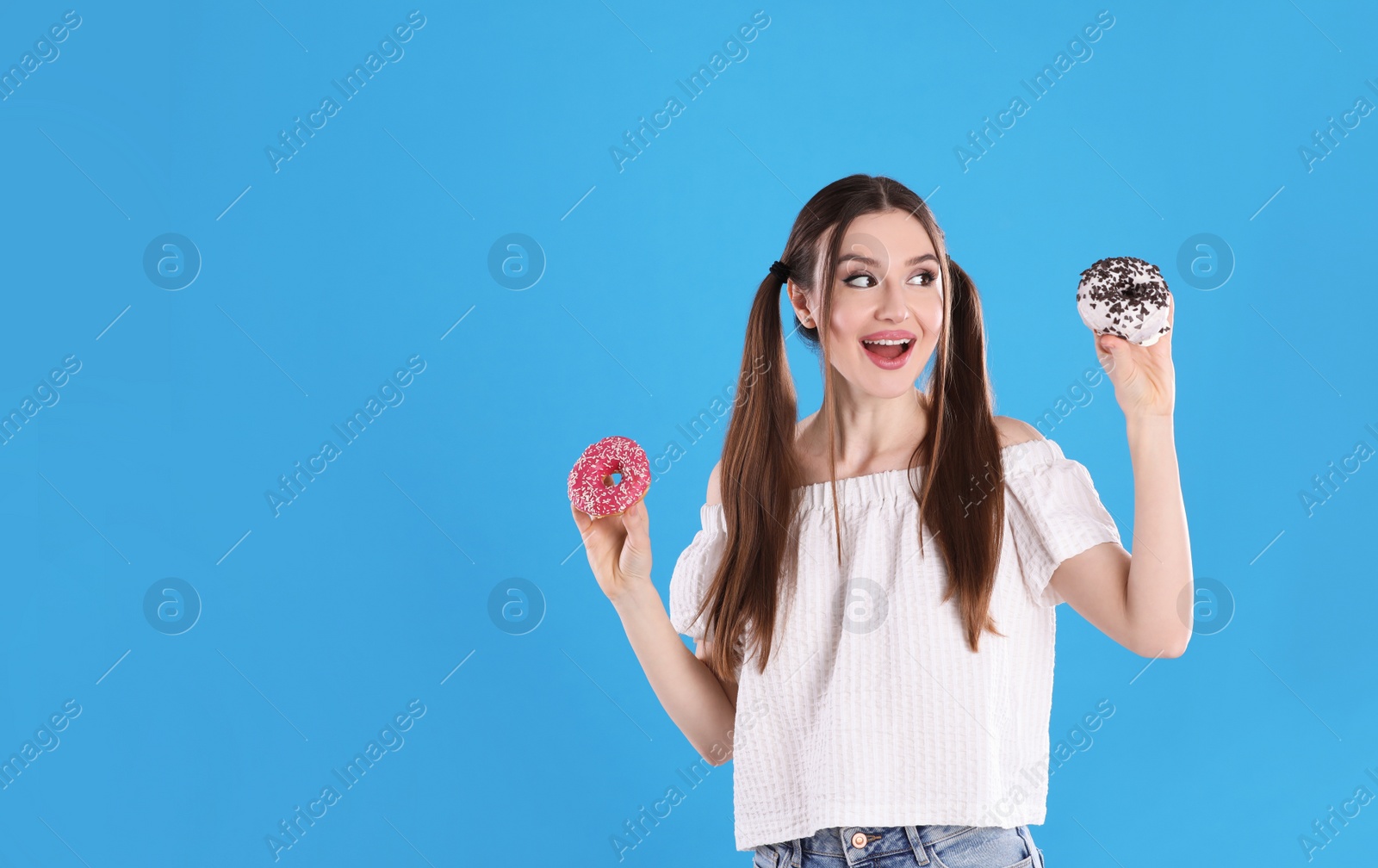 Photo of Beautiful young woman with donuts on light blue background