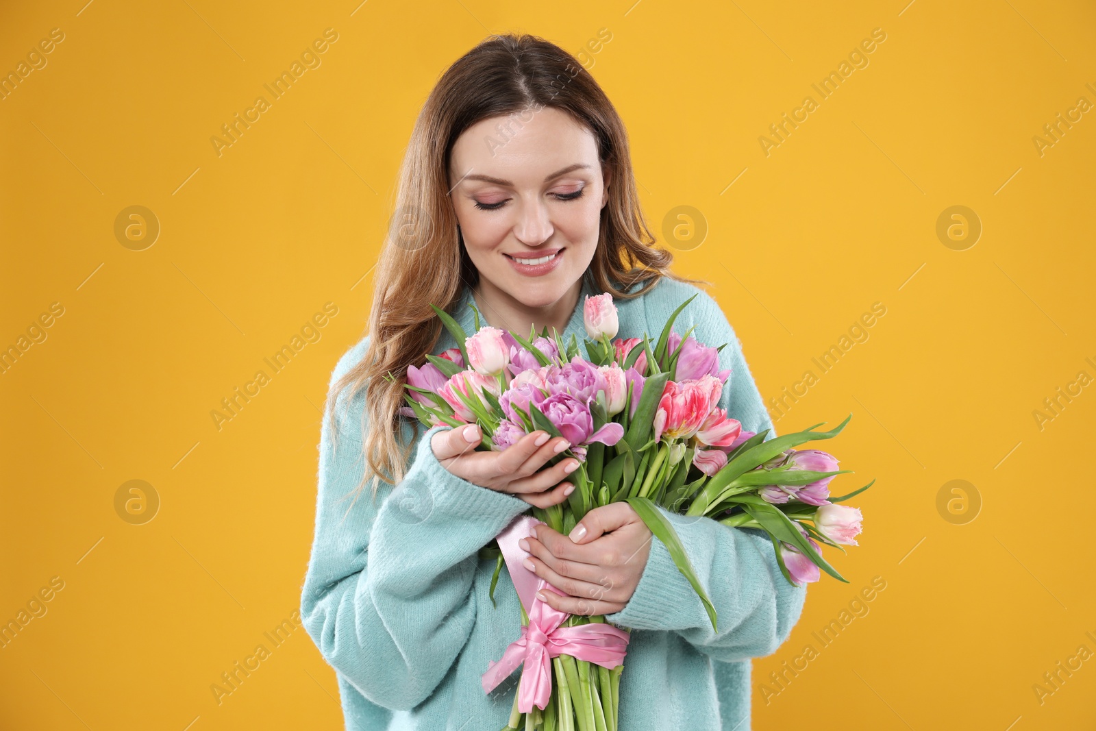 Photo of Happy young woman with bouquet of beautiful tulips on yellow background