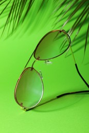 Photo of Stylish sunglasses and palm branches on green background