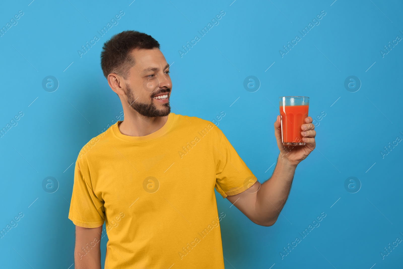 Photo of Man holding glass of delicious juice on light blue background