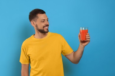 Photo of Man holding glass of delicious juice on light blue background