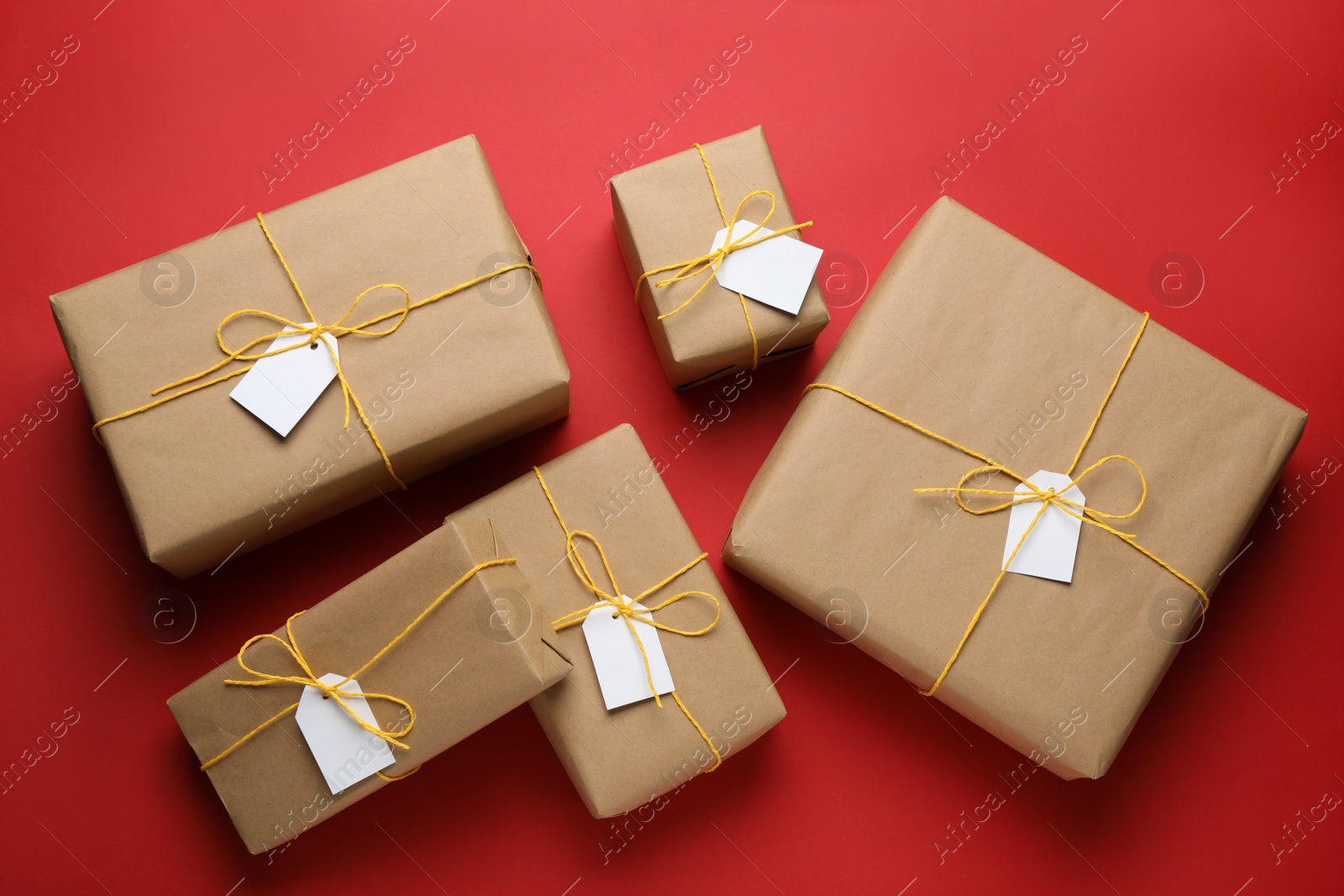 Photo of Parcels wrapped in kraft paper with tags on red background, flat lay