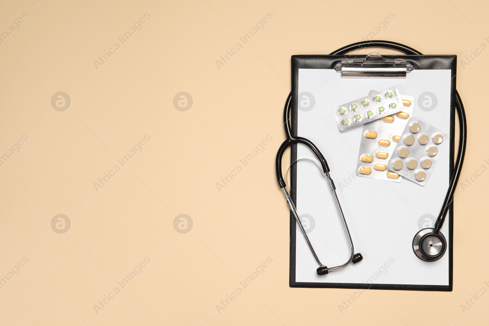 Photo of Stethoscope, pills and clipboard on beige background, top view. Space for text