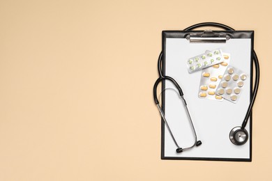 Stethoscope, pills and clipboard on beige background, top view. Space for text