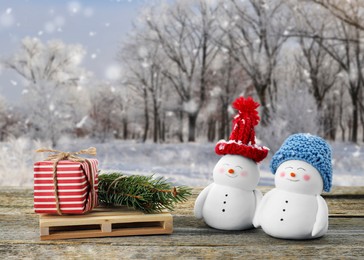 Image of Cute decorative snowmen, gift box and fir tree branches on wooden table outdoors