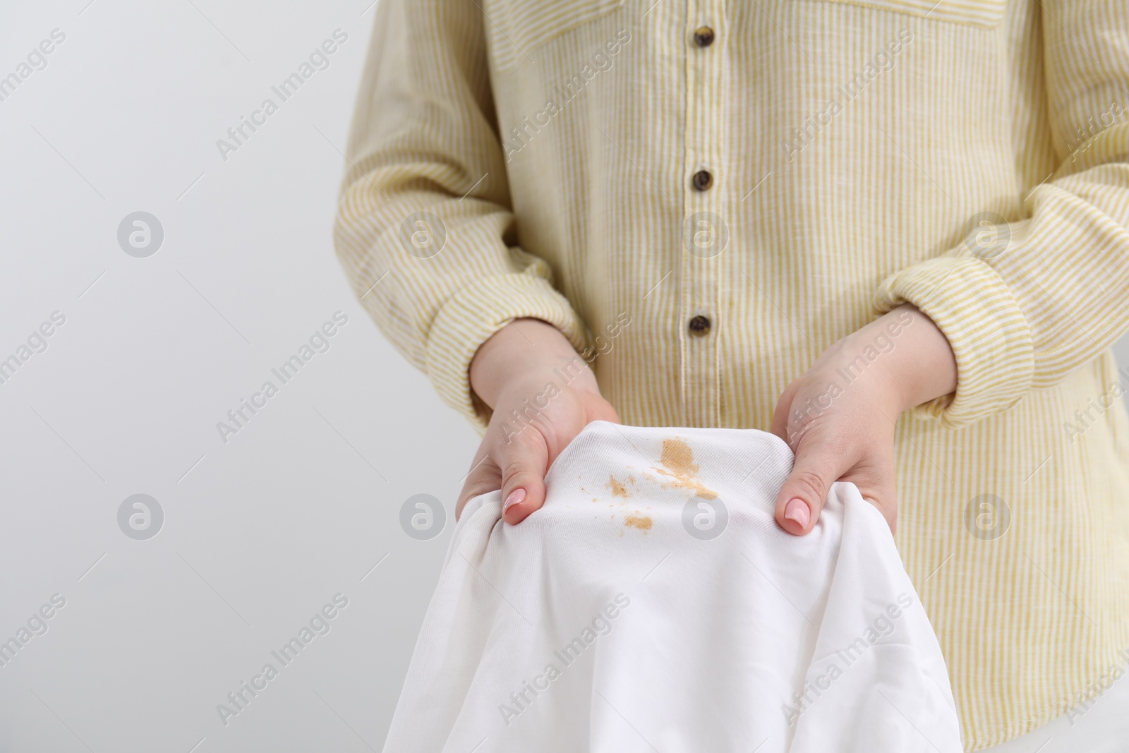 Photo of Woman holding shirt with stain against light background, closeup. Space for text