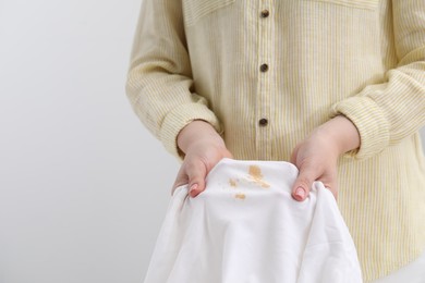 Woman holding shirt with stain against light background, closeup. Space for text