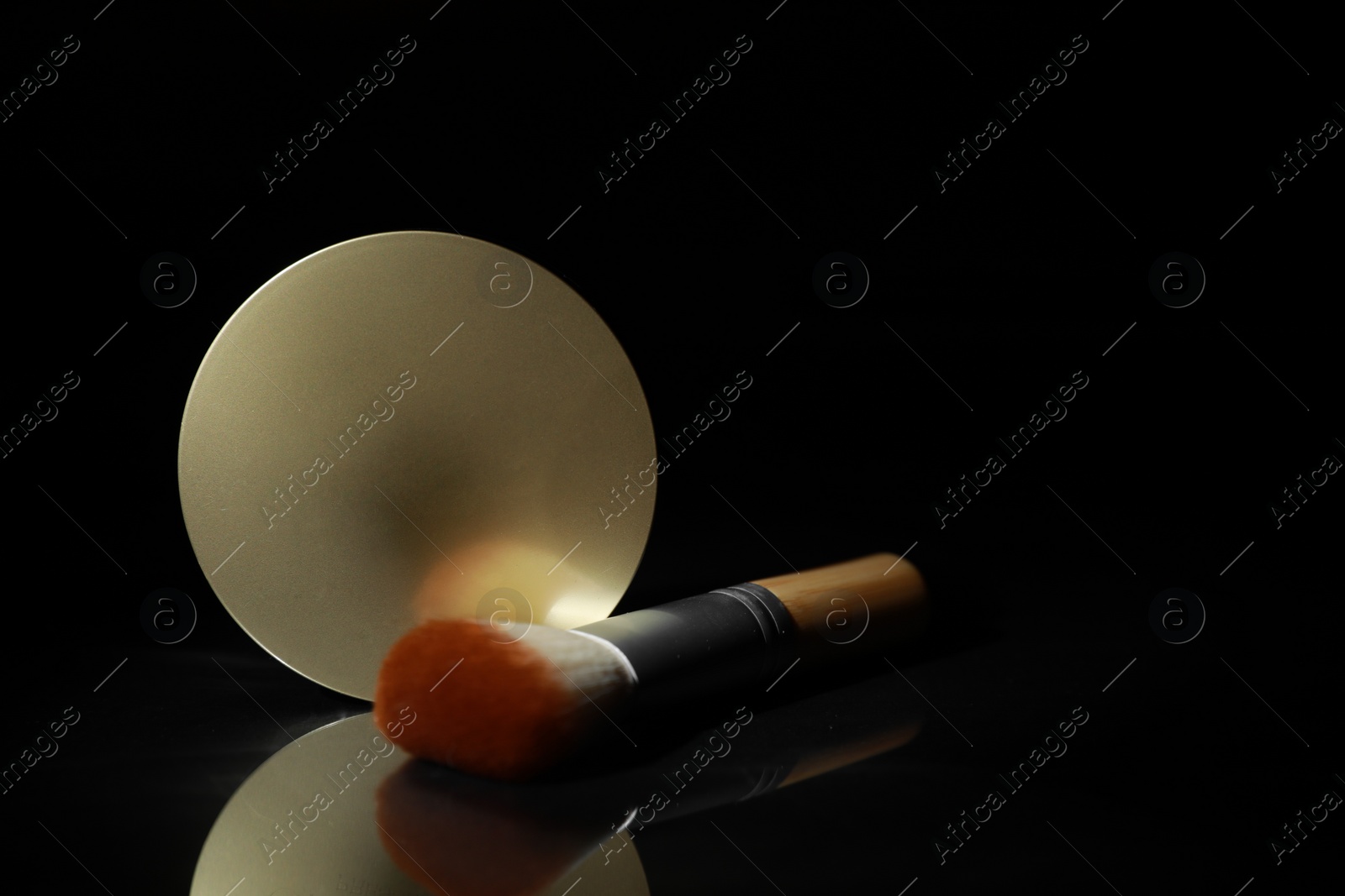 Photo of Face powder and makeup brush on black mirror surface in darkness, closeup. Space for text