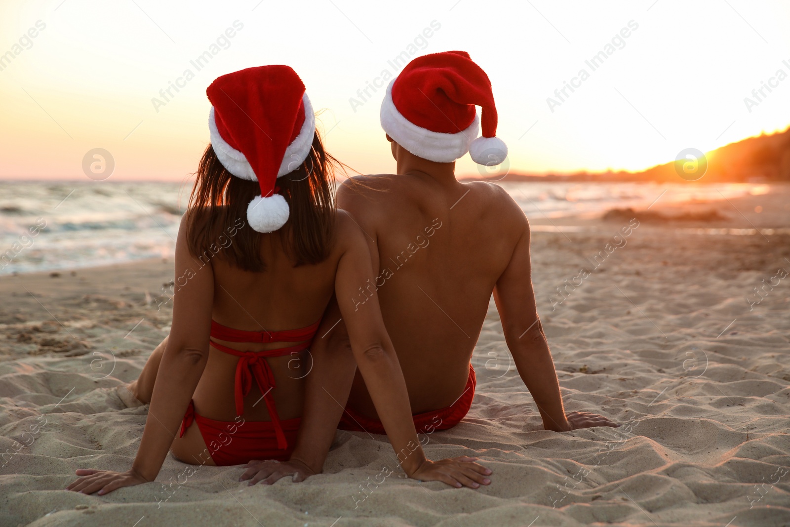 Photo of Lovely couple with Santa hats together on beach at sunset, back view. Christmas vacation