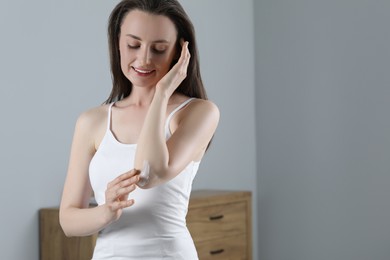 Photo of Happy woman applying body cream onto elbow indoors, space for text