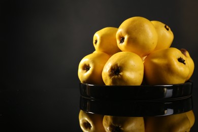Photo of Tasty ripe quinces in bowl on black mirror surface, space for text