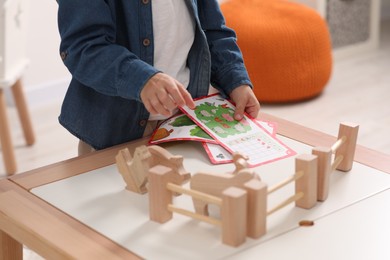 Little boy playing with set of wooden animals and fence at table indoors, closeup. Child's toy