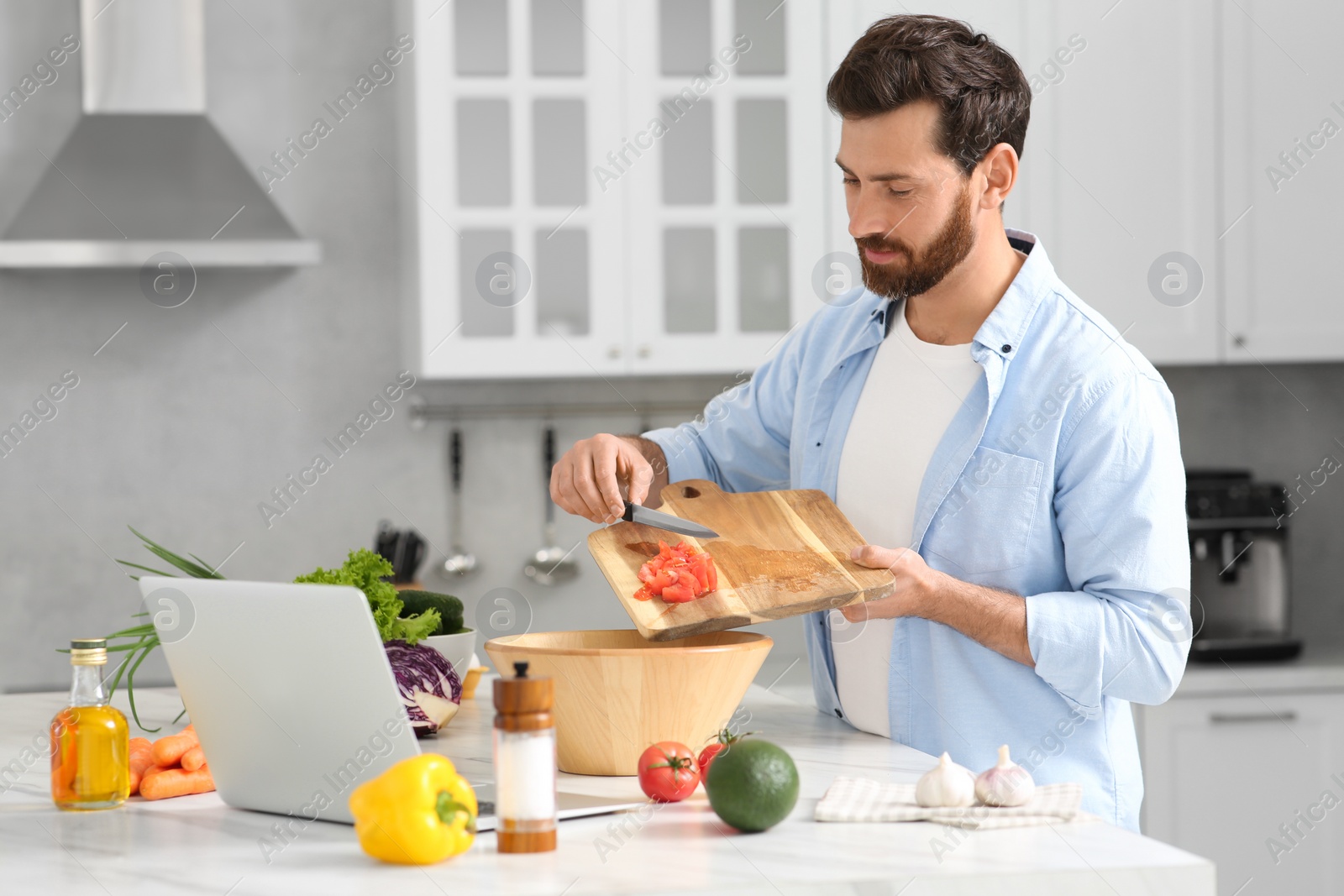 Photo of Man making dinner while watching online cooking course via laptop in kitchen