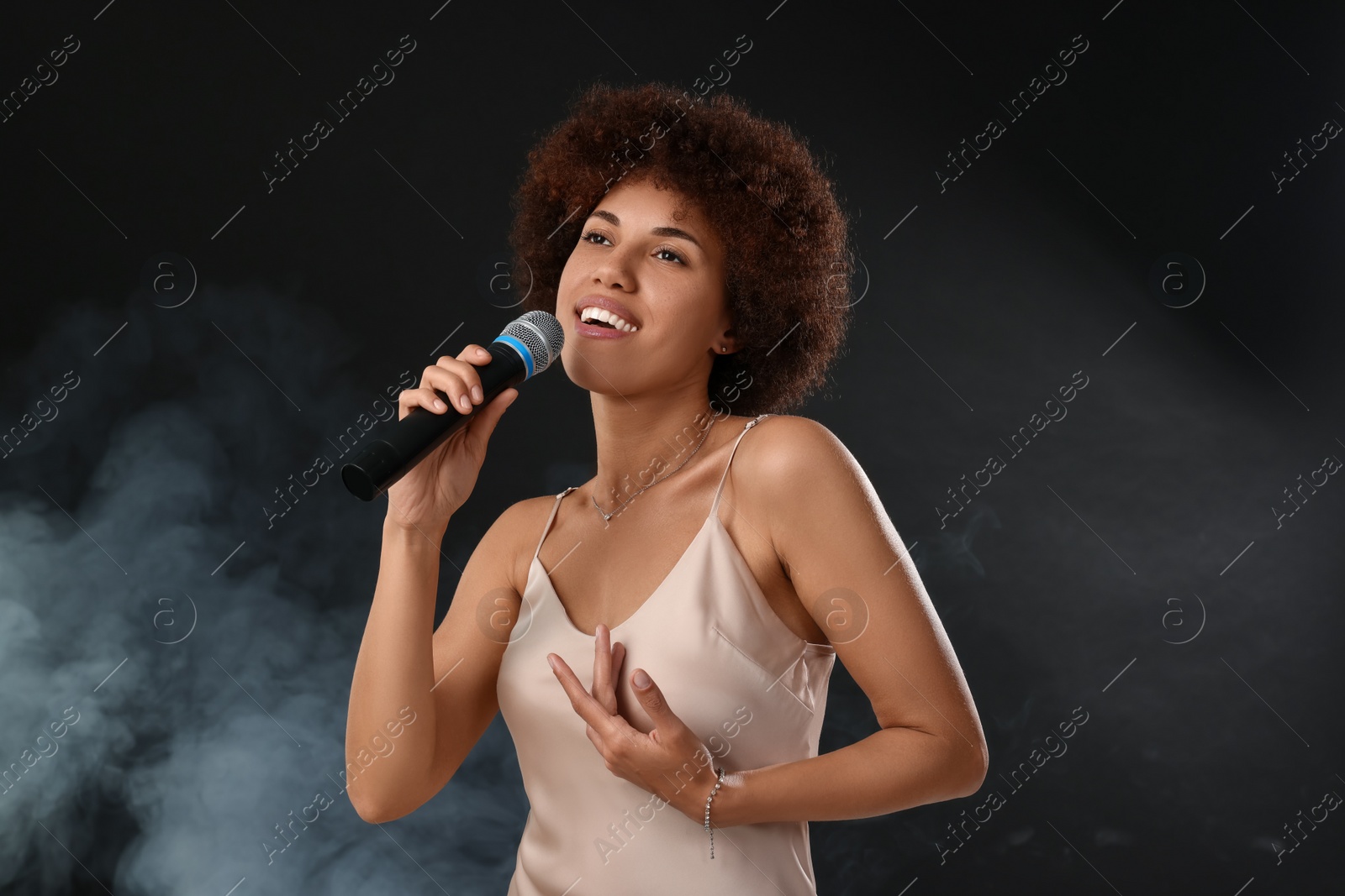 Photo of Curly young woman with microphone singing in smoke on black background