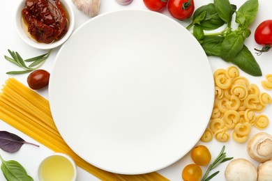 Photo of Plate surrounded by different types of pasta and products on white background, flat lay. Space for text