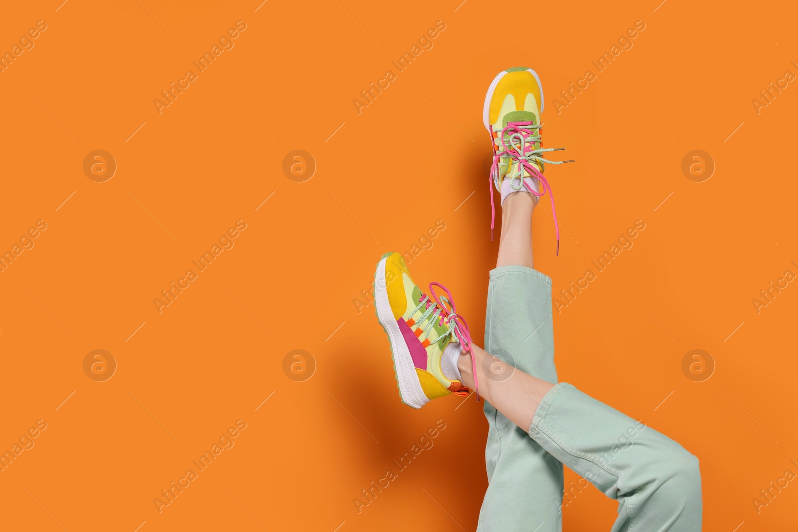 Photo of Woman wearing pair of new stylish sneakers on orange background, closeup. Space for text