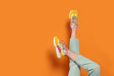 Photo of Woman wearing pair of new stylish sneakers on orange background, closeup. Space for text