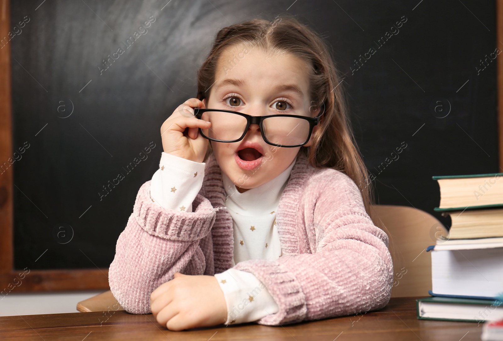 Photo of Cute little child wearing glasses at desk in classroom. First time at school