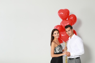 Beautiful couple with heart shaped balloons on light background, space for text