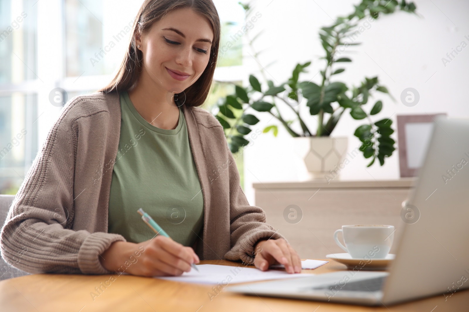 Photo of Woman writing letter at wooden table in room